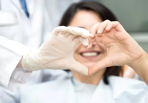 A happy patient and dentist making a heart with their hands