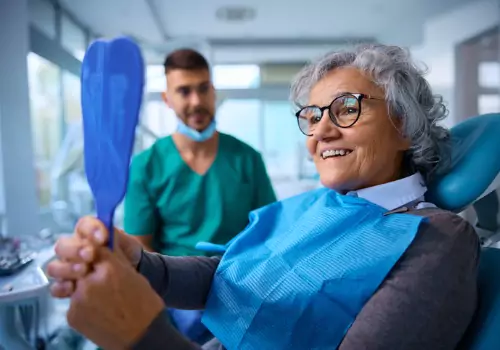 A happy elderly woman admiring her teeth after receiving dental work from a Dentist in Pekin IL