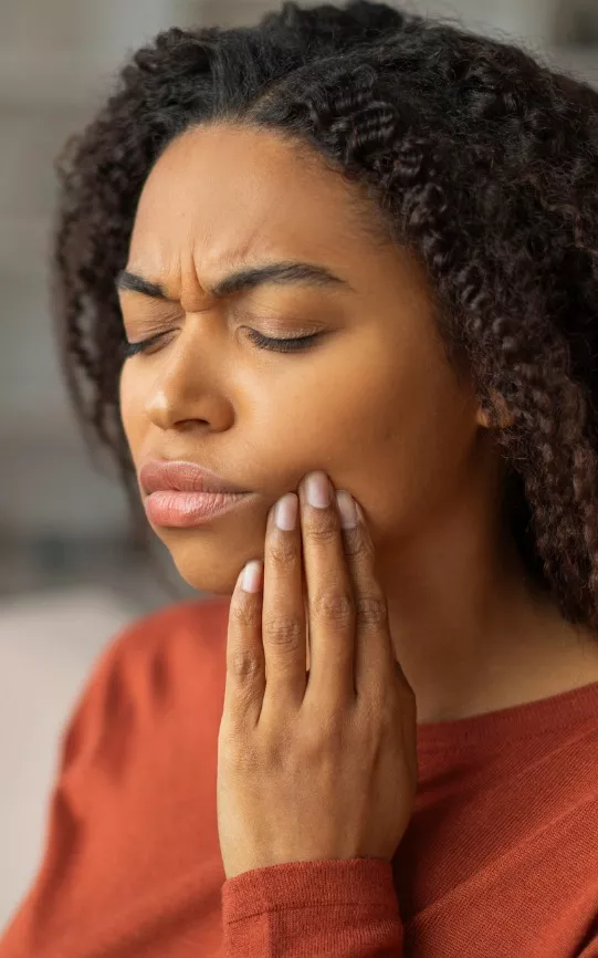 Young woman holding the side of her mouth because of tooth pain, requiring dental services from Total Dental Care