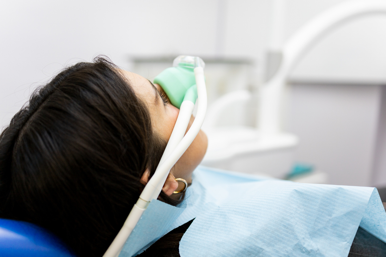 A woman sits in a dentist’s chair, inhaling nitrous oxide, after contacting Total Dental Care about one of her dental emergencies