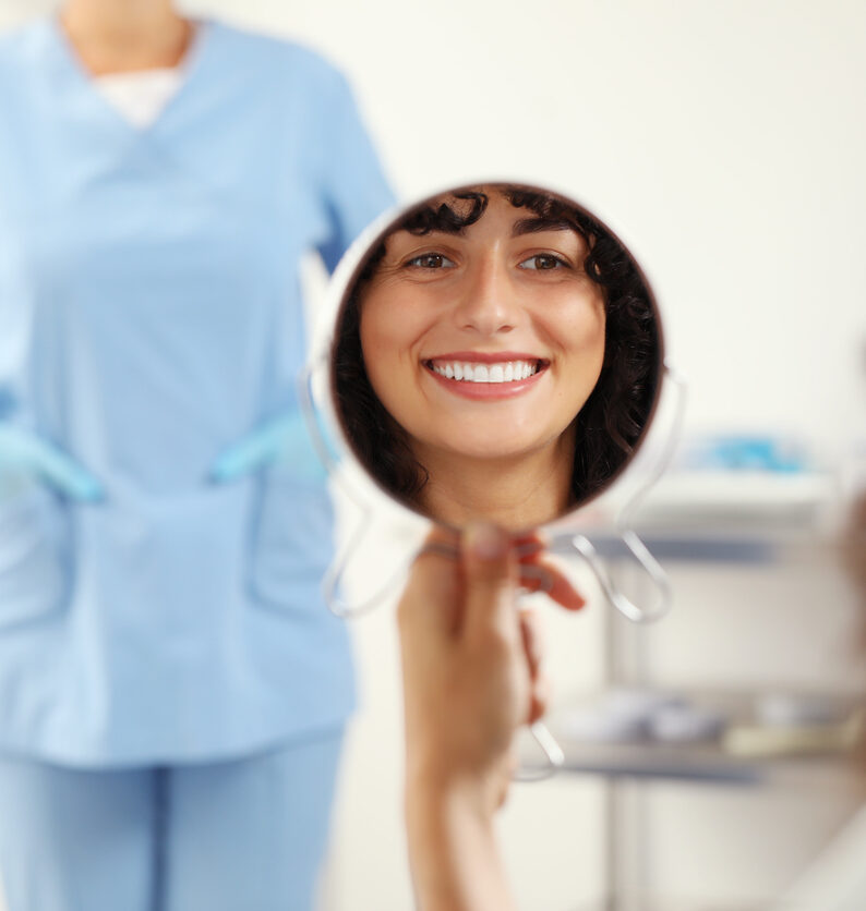 A happy woman smiles in the mirror at the dentist after getting dental crowns